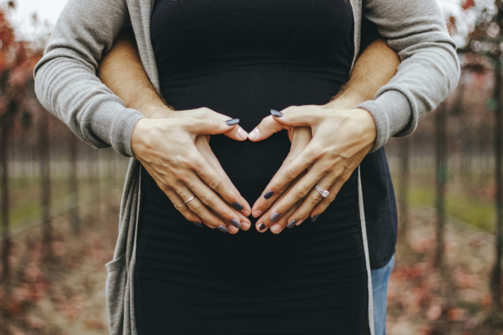 Man and woman embracing, forming a heart shape with their hands over her baby bump.