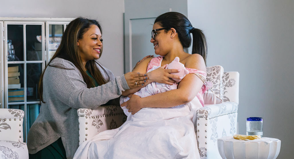 A new mother feeds her baby while a doula provides gentle support