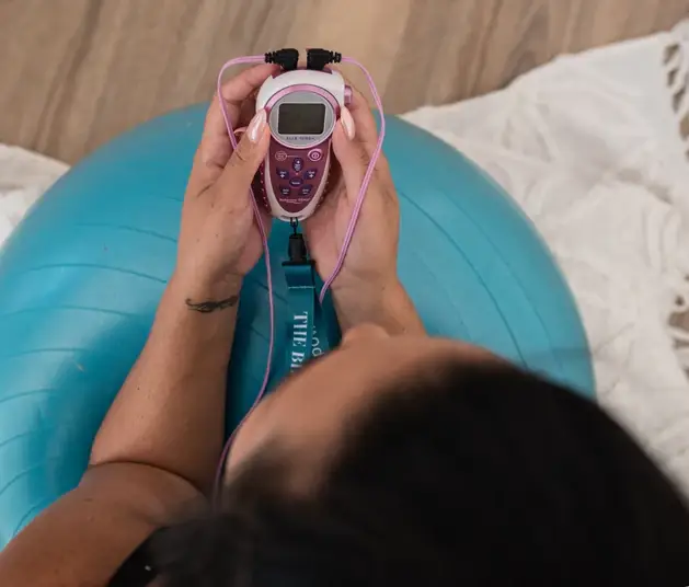 Laboring mother using a TENS unit for pain relief while sitting on a birth ball