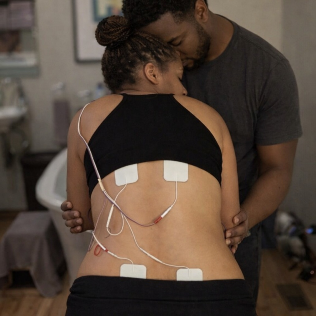 Laboring mother using a TENS unit on her lower back while leaning on her partner for support