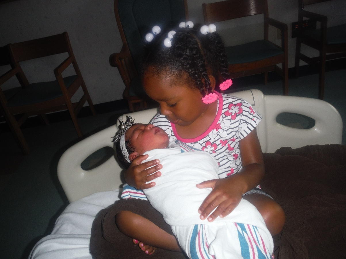 Young big sister holding her newborn baby sibling for the first time in the hospital