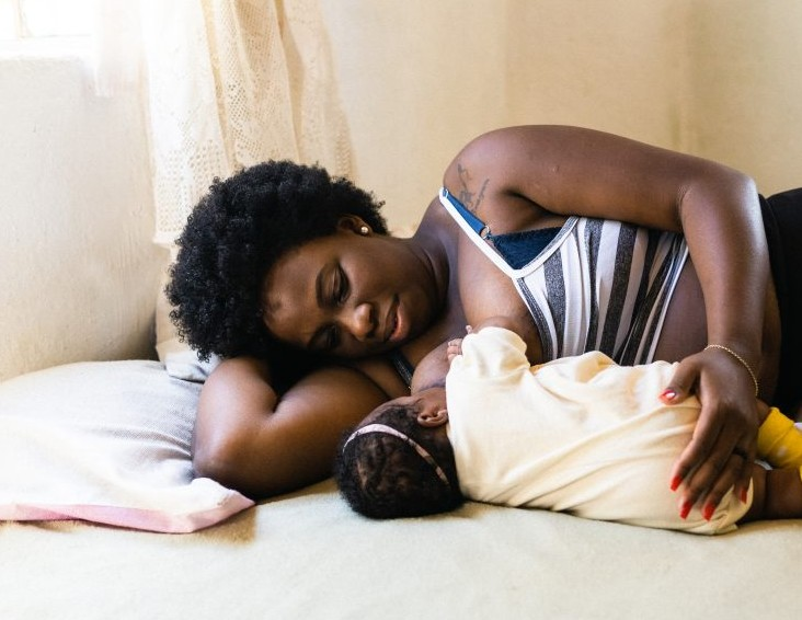 Mother breastfeeding her newborn in a side-lying position during the first days postpartum