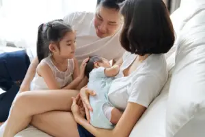 Older daughter gently touching newborn baby while sitting with parents during family transition after birth