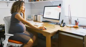 Pregnant woman working at a desk in a home office while balancing job responsibilities during pregnancy