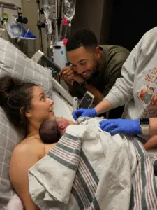 New parents meeting their baby during the Golden Hour while a nurse provides postpartum care in the hospital.