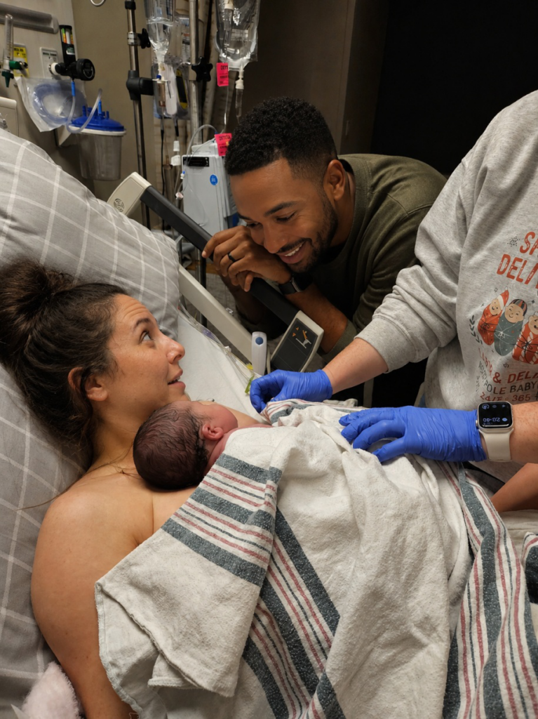 New parents meeting their baby during the Golden Hour while a nurse provides postpartum care in the hospital.