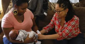 Postpartum doula showing a new mother newborn care techniques during an in-home postpartum visit.