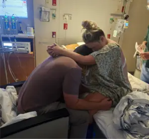 Laboring mother leaning on her partner for support in a hospital room after unexpected changes to her birth plan