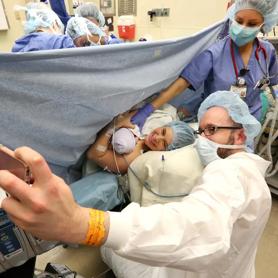 Mother meeting her newborn baby during a C-section birth in the operating room with her support person beside her